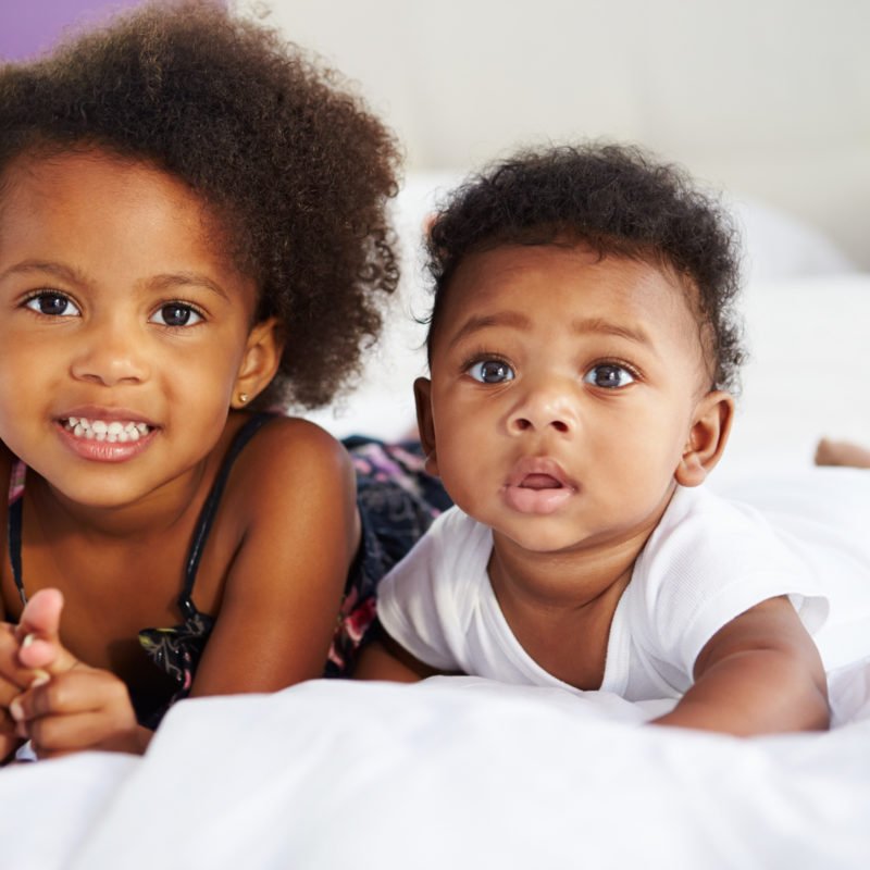 Sister With Baby Brother Lying On Parent's Bed